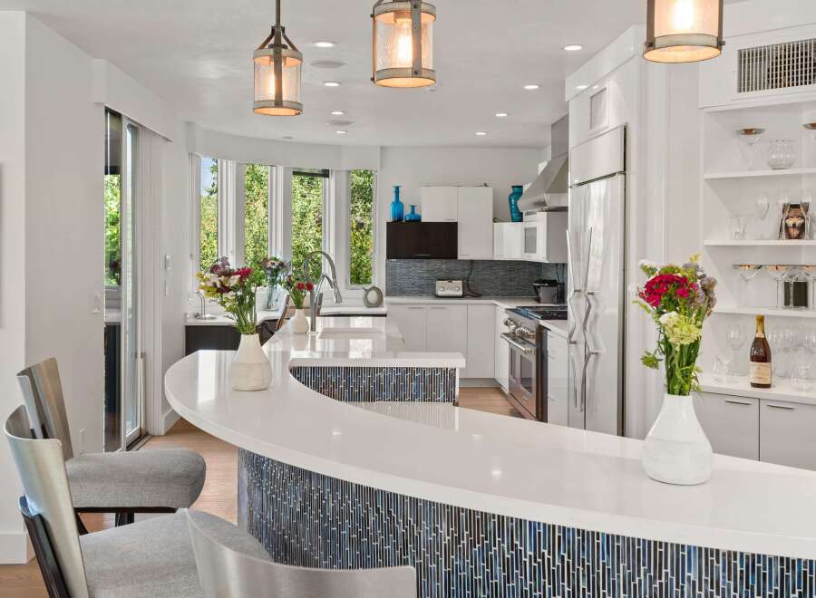Experience modern luxury in this stunning kitchen, featuring a sleek white countertop island with a captivating blue mosaic tile base.