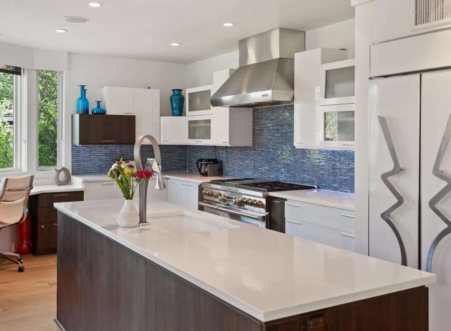 Experience modern luxury in this stunning kitchen featuring sleek white cabinetry, a striking blue mosaic tile backsplash, and a spacious island with a built-in sink.