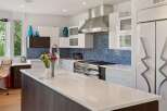 Experience modern luxury in this stunning kitchen featuring sleek white cabinetry, a striking blue mosaic tile backsplash, and a spacious island with a built-in sink.