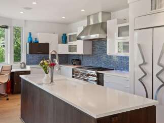 Experience modern luxury in this stunning kitchen featuring sleek white cabinetry, a striking blue mosaic tile backsplash, and a spacious island with a built-in sink.
