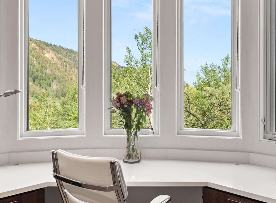 Enjoy breathtaking mountain views from this elegant home office featuring a spacious built-in desk and a comfortable white leather executive chair.
