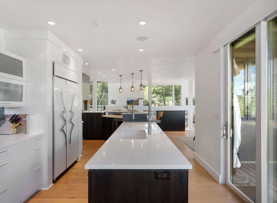 Experience modern luxury in this stunning kitchen, featuring sleek white cabinetry, a large waterfall island with a sink, and high-end stainless steel appliances.