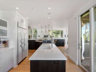 Experience modern luxury in this stunning kitchen, featuring sleek white cabinetry, a large waterfall island with a sink, and high-end stainless steel appliances.
