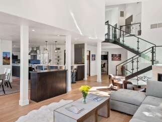 Experience modern luxury in this stunning open-concept living space, featuring a sleek kitchen with a central island and a dramatic floating staircase with glass railings.