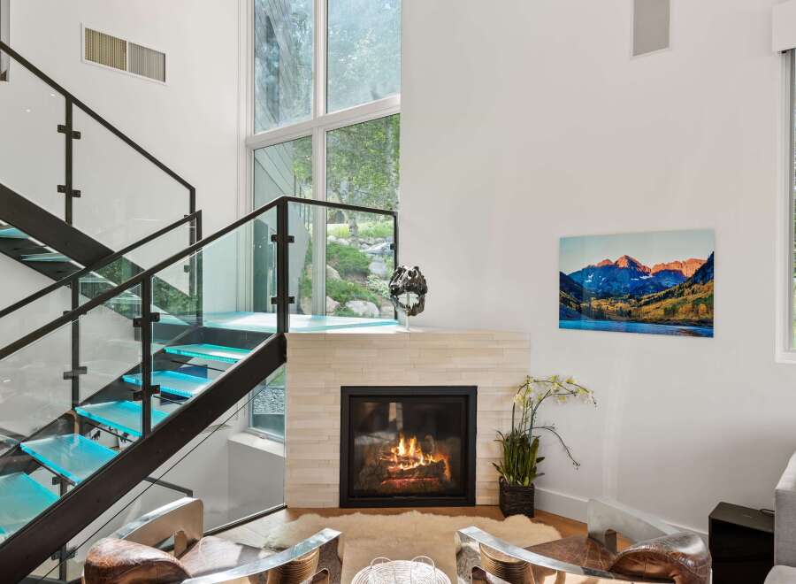 Experience modern luxury in this stunning living room, featuring a striking glass and metal staircase with illuminated blue treads.