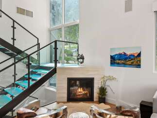 Experience modern luxury in this stunning living room, featuring a striking glass and metal staircase with illuminated blue treads.