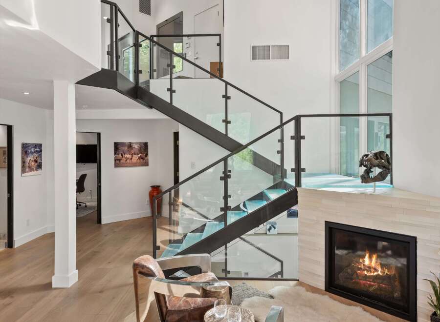 Experience modern luxury in this stunning living space, featuring a dramatic floating staircase with glass railings and a sleek fireplace.