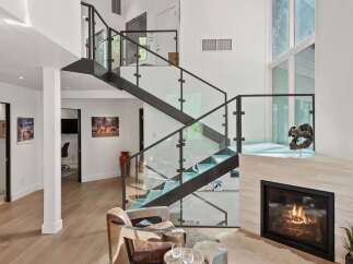 Experience modern luxury in this stunning living space, featuring a dramatic floating staircase with glass railings and a sleek fireplace.
