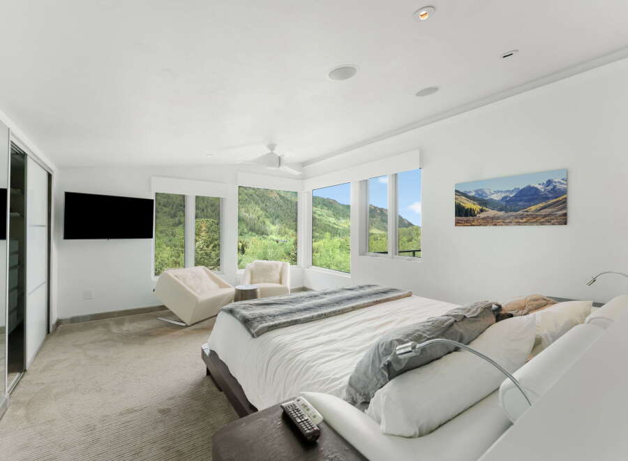 Experience luxury mountain living in this stunning bedroom featuring panoramic views of lush green hills and snow-capped peaks through expansive windows.