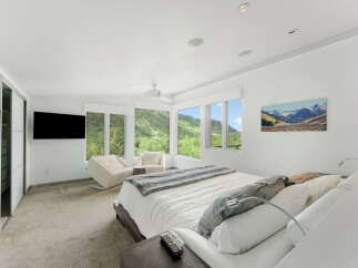 Experience luxury mountain living in this stunning bedroom featuring panoramic views of lush green hills and snow-capped peaks through expansive windows.
