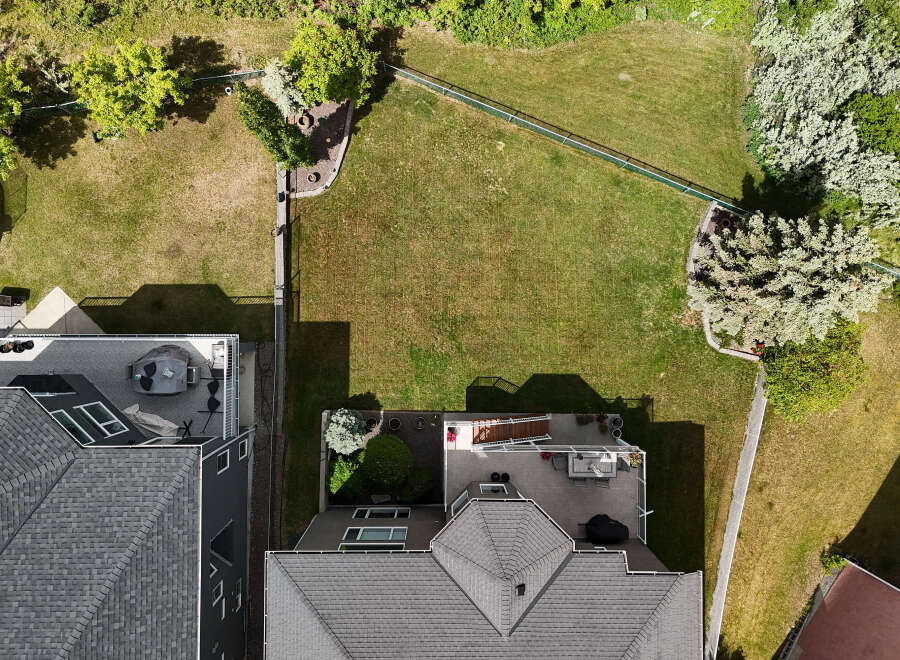 Discover this stunning aerial view showcasing a beautifully landscaped backyard with lush green grass, mature trees, and a charming garden area.