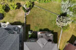 Discover this stunning aerial view showcasing a beautifully landscaped backyard with lush green grass, mature trees, and a charming garden area.