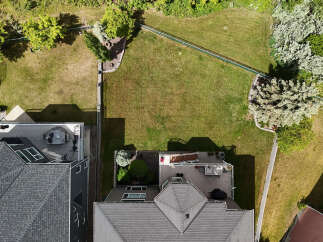 Discover this stunning aerial view showcasing a beautifully landscaped backyard with lush green grass, mature trees, and a charming garden area.