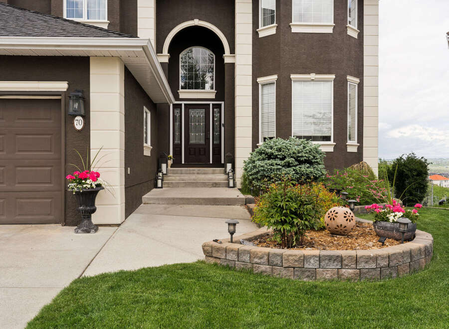 This stunning home features a grand entrance with a large arched window and a dark wood door, complemented by elegant landscaping.