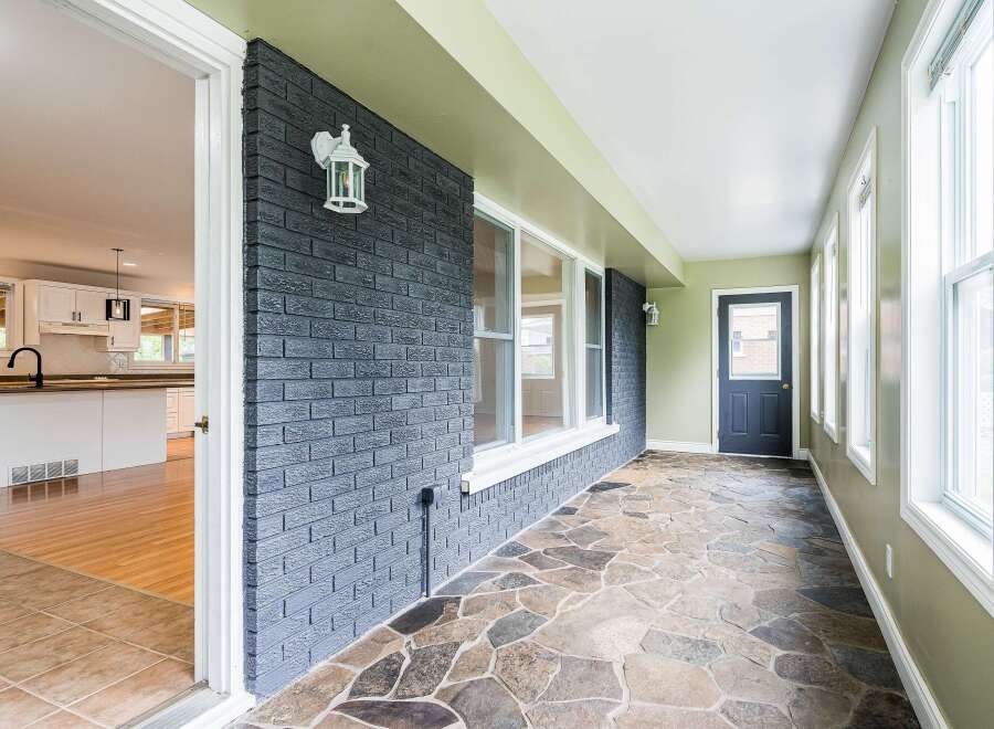 Step into this charming sunroom, featuring a unique flagstone floor and a striking dark brick accent wall.
