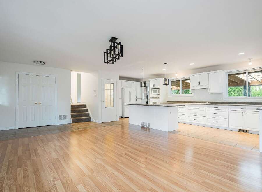 Discover this beautifully renovated open-concept living space, featuring a modern white kitchen with ample cabinet storage and a central island perfect for entertaining.