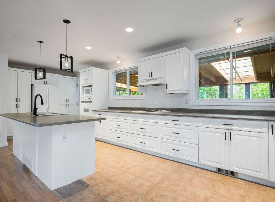 This spacious white kitchen features a large island with a sink and faucet, complemented by ample cabinet and drawer space for all your storage needs.