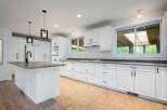 This spacious white kitchen features a large island with a sink and faucet, complemented by ample cabinet and drawer space for all your storage needs.