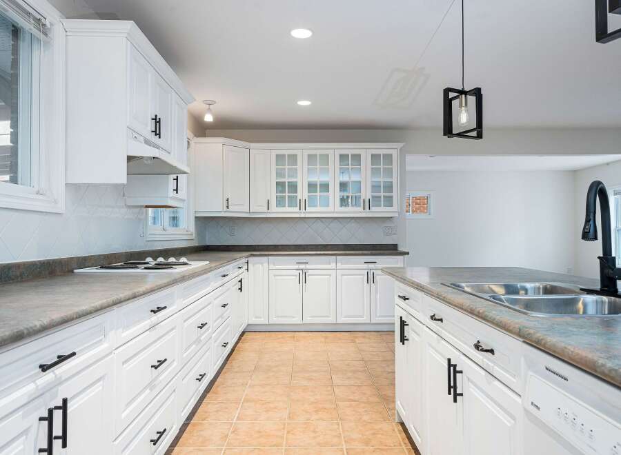 This spacious kitchen boasts pristine white cabinetry with elegant black hardware, complemented by a sleek countertop and a diamond-patterned tile backsplash.