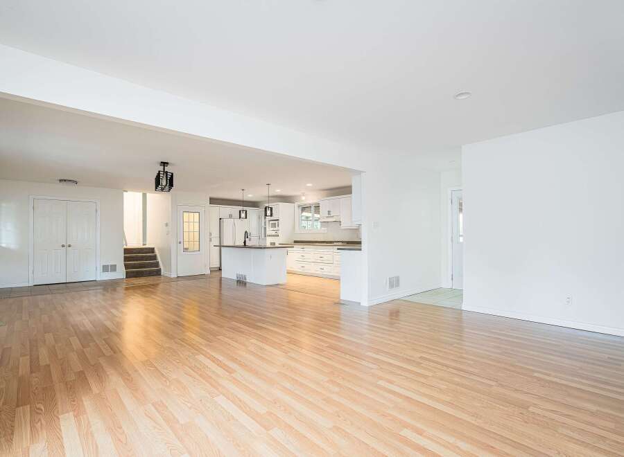 Step into this bright and airy open-concept living space, featuring gleaming hardwood floors that flow seamlessly into a modern white kitchen.