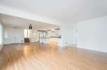 Step into this bright and airy open-concept living space, featuring gleaming hardwood floors that flow seamlessly into a modern white kitchen.