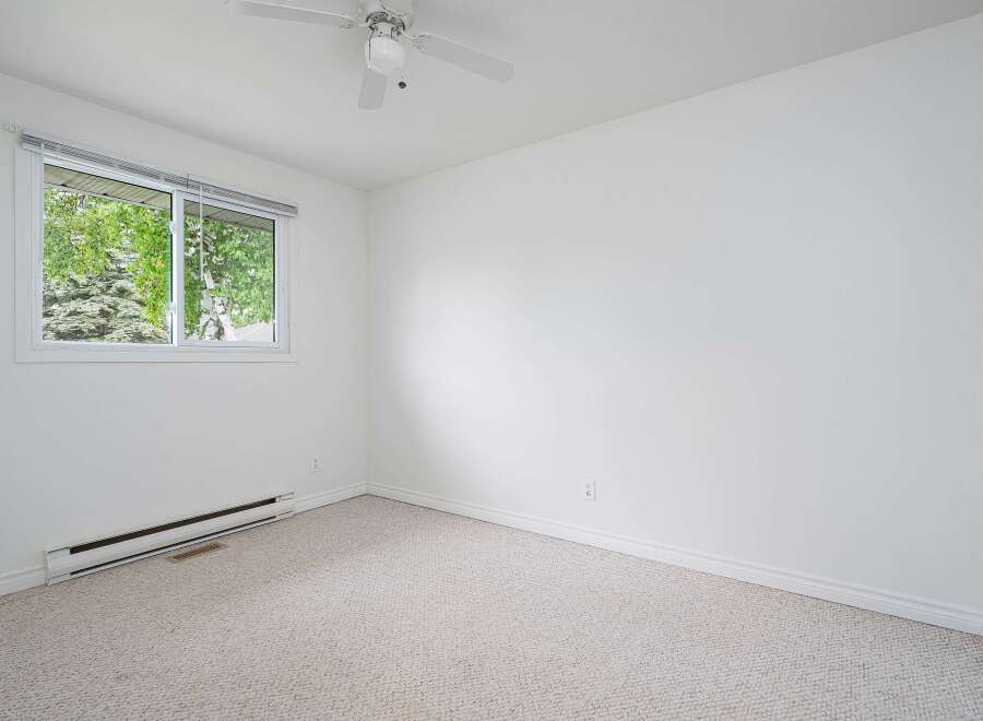 This bright and airy bedroom features a large window offering abundant natural light and views of lush greenery.