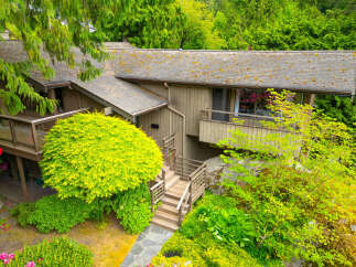 Nestled amidst lush greenery, this charming home offers a serene retreat with its natural wood siding and expansive decks perfect for outdoor living.