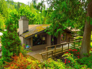 Nestled amidst lush greenery, this charming home offers a serene retreat with its expansive wooden deck and natural surroundings.