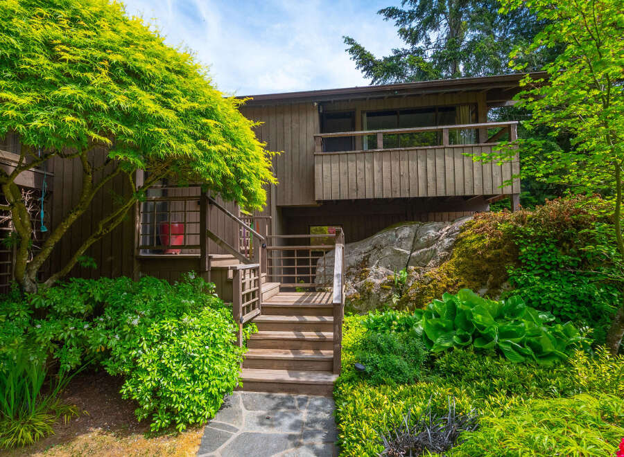 Nestled amidst lush greenery, this charming home features a multi-level wooden deck and staircase leading to the entrance.