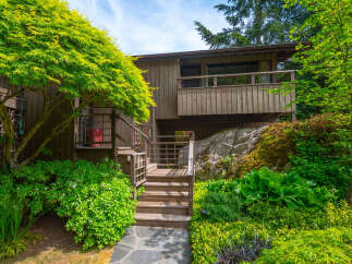 Nestled amidst lush greenery, this charming home features a multi-level wooden deck and staircase leading to the entrance.