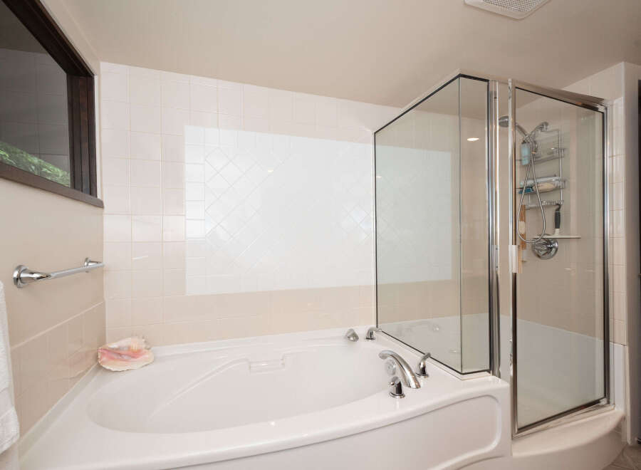 Indulge in relaxation with this luxurious corner bathtub, featuring a separate glass-enclosed shower for ultimate convenience.