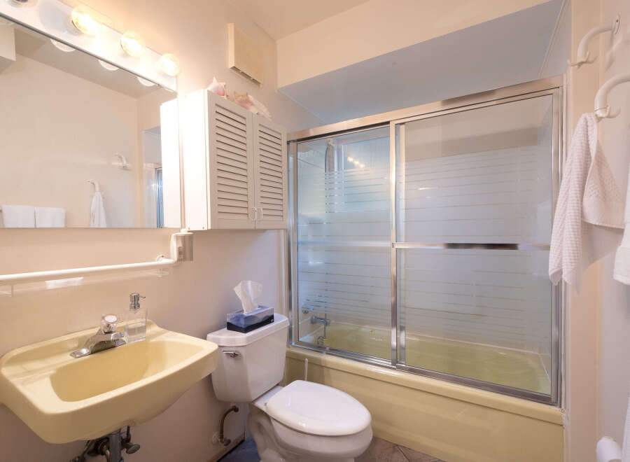 This bathroom features a light yellow bathtub with a frosted glass sliding door, a white toilet with a tissue box, and a matching sink with a chrome faucet.