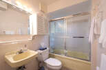This bathroom features a light yellow bathtub with a frosted glass sliding door, a white toilet with a tissue box, and a matching sink with a chrome faucet.