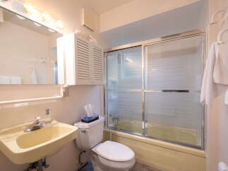 This bathroom features a light yellow bathtub with a frosted glass sliding door, a white toilet with a tissue box, and a matching sink with a chrome faucet.