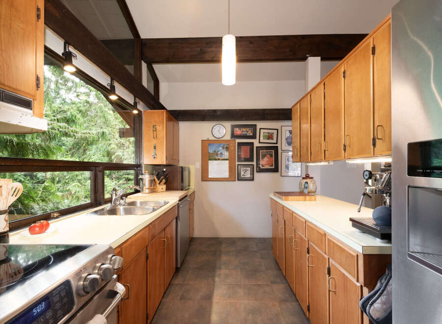 Experience the charm of this kitchen, featuring warm wooden cabinetry and a spacious double sink overlooking a lush green forest view.