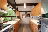 Experience the charm of this kitchen, featuring warm wooden cabinetry and a spacious double sink overlooking a lush green forest view.