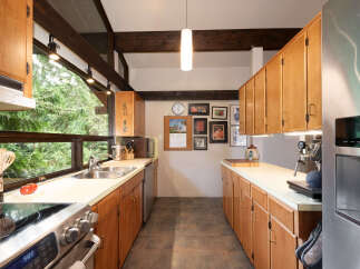 Experience the charm of this kitchen, featuring warm wooden cabinetry and a spacious double sink overlooking a lush green forest view.