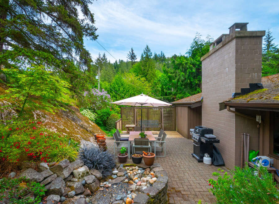 Enjoy outdoor living with this charming patio featuring a dining set under a large umbrella, a built-in barbecue grill, and a cozy swing set.
