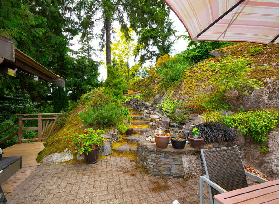 Discover this stunning outdoor oasis, featuring a multi-level stone pathway winding through lush greenery and leading to a charming wooden deck.