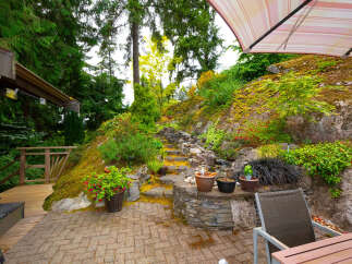 Discover this stunning outdoor oasis, featuring a multi-level stone pathway winding through lush greenery and leading to a charming wooden deck.
