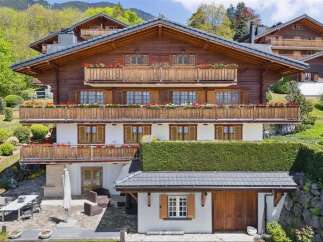 Experience luxury mountain living in this stunning chalet, featuring multiple balconies adorned with vibrant flower boxes and expansive windows offering breathtaking views.