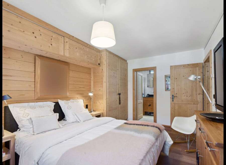 Experience rustic charm in this cozy bedroom featuring warm, wood-paneled walls and a comfortable bed adorned with plush white linens.