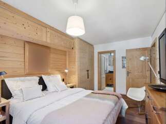 Experience rustic charm in this cozy bedroom featuring warm, wood-paneled walls and a comfortable bed adorned with plush white linens.