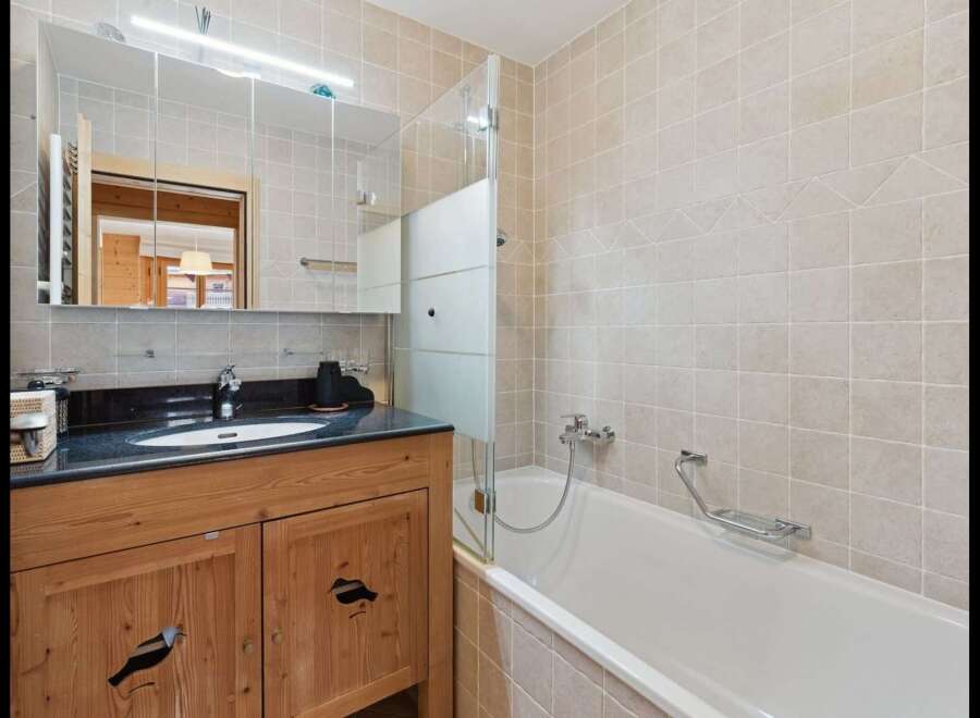 This charming bathroom features a rustic wooden vanity with intricate bird carvings, complemented by a sleek granite countertop and a modern undermount sink.
