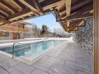 Experience luxury in this stunning alpine retreat featuring an outdoor swimming pool surrounded by snow-covered landscapes.
