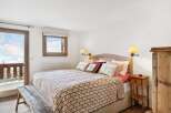 Experience cozy mountain living in this charming bedroom featuring a comfortable bed adorned with decorative pillows and a rustic quilt.