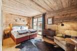 Experience rustic luxury in this charming bedroom, featuring warm wood paneling throughout and a cozy king-sized bed adorned with plush linens and decorative throws.