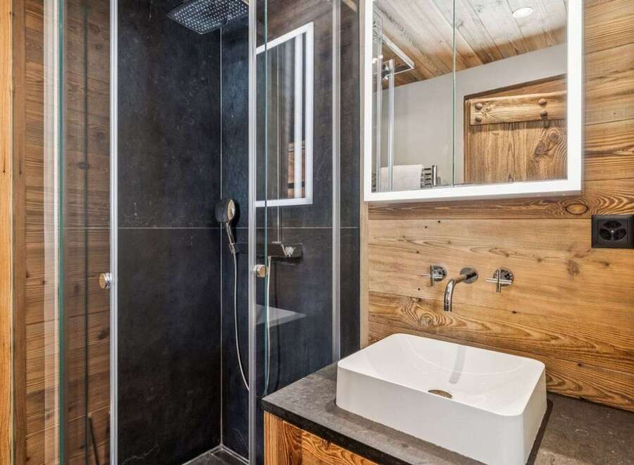 Experience modern alpine living in this beautifully appointed bathroom, featuring a sleek glass-enclosed shower with a rainfall showerhead and dark stone tiling.