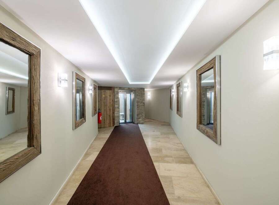 Step into this elegant hallway featuring a plush brown carpet runner leading to a modern elevator and rustic wooden doors.