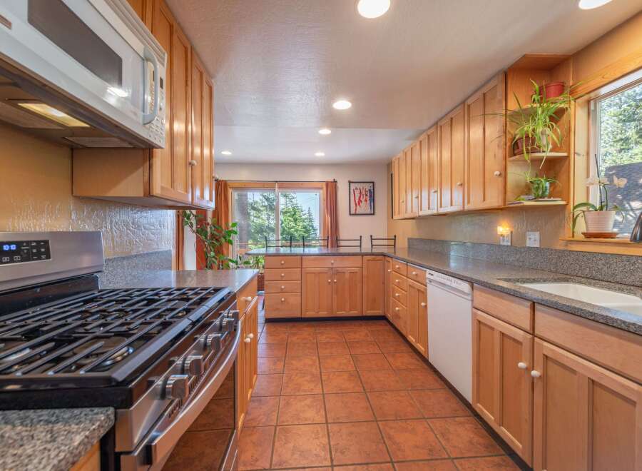 This spacious kitchen features light wood cabinetry, granite countertops, and a gas range perfect for cooking enthusiasts.